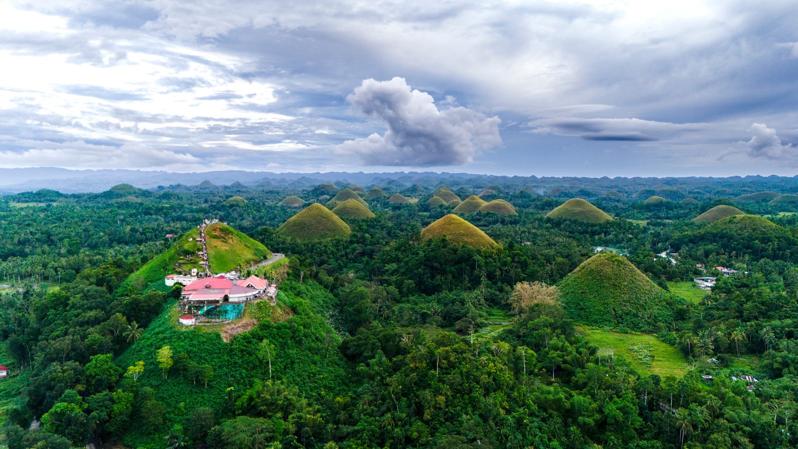 The Chocolate Hills from the air in wet-season green, the viewing complex at Carmen on one summit.
