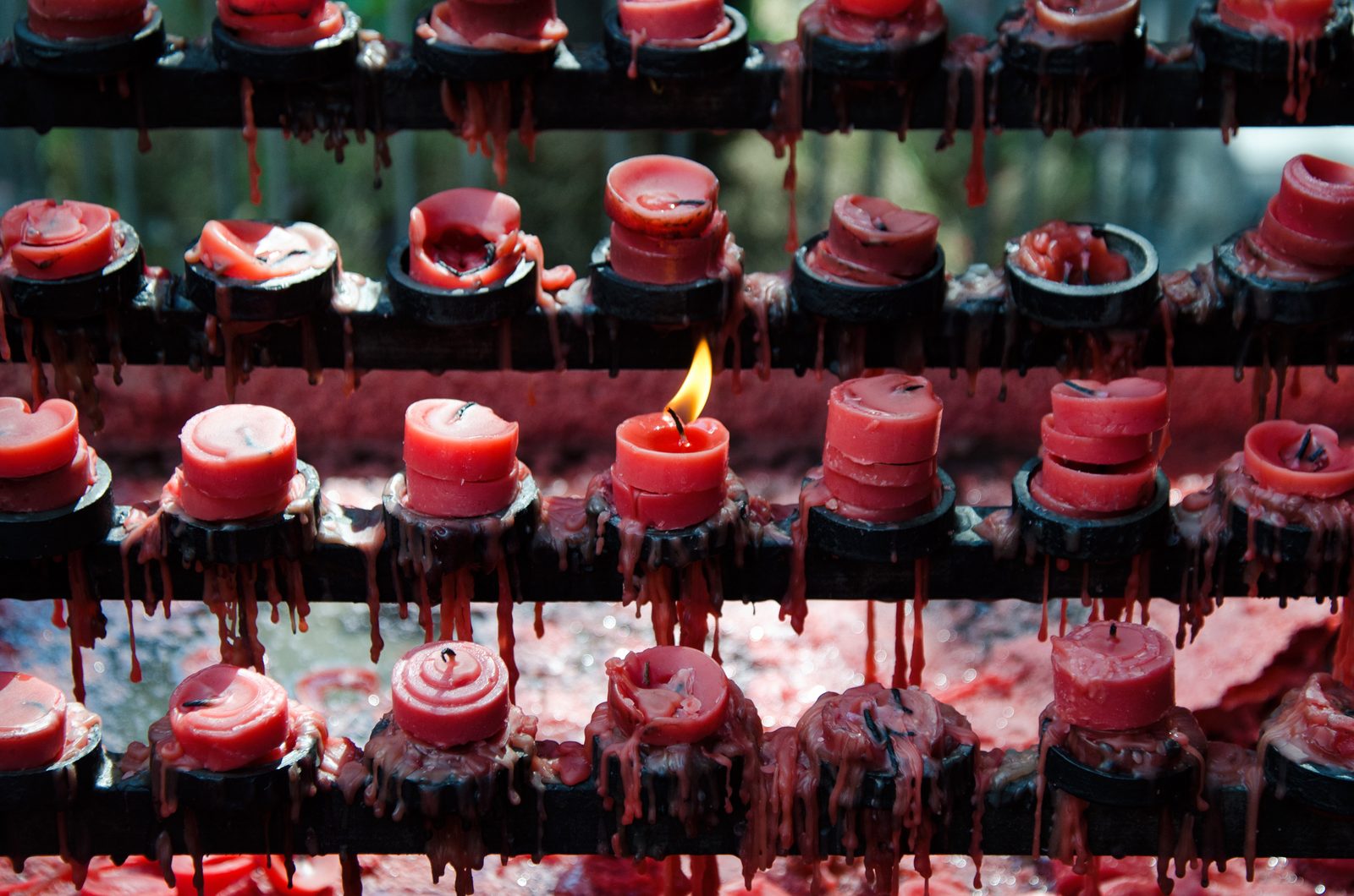 Racks of red devotional candles at the Basilica del Santo Ni&ntilde;o, one flame alight, wax pooling below.