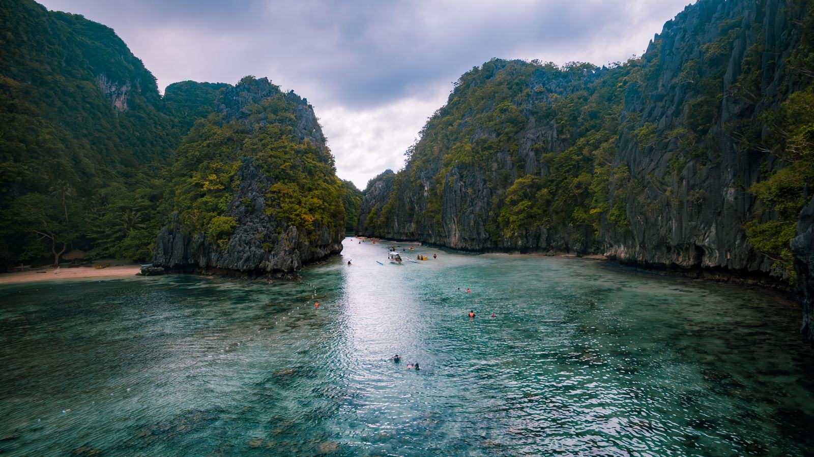 An enclosed cove in the Bacuit archipelago, swimmers in green water ringed by limestone.