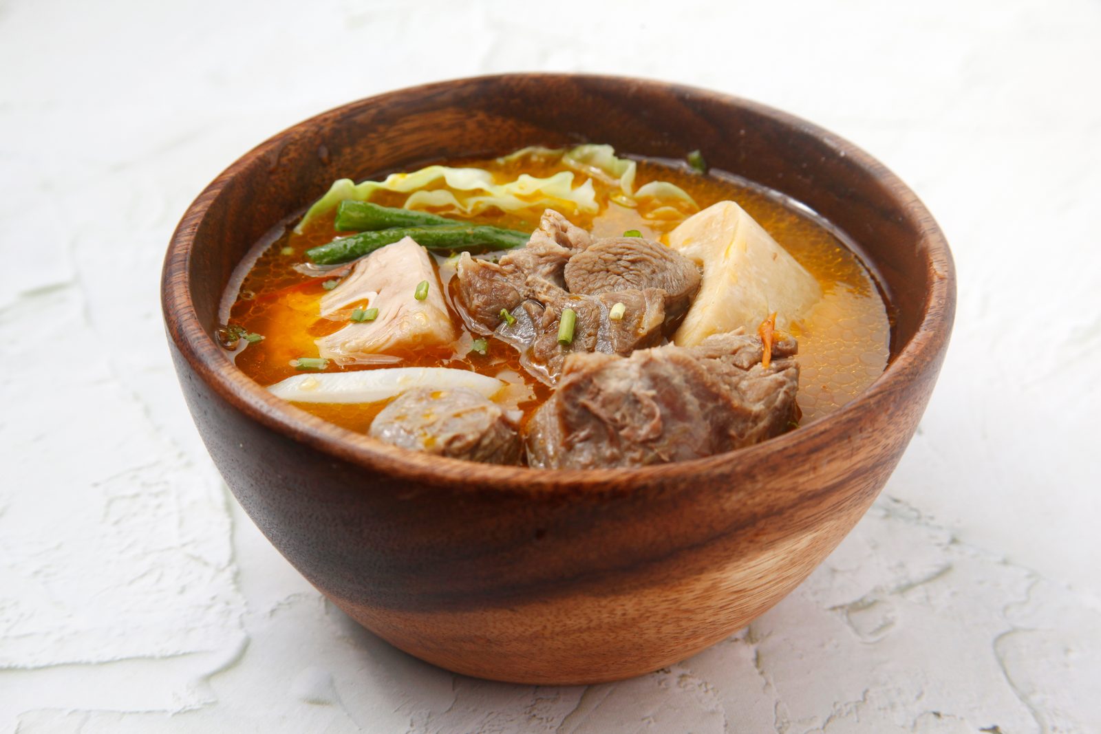 A wooden bowl of kansi: beef shank and vegetables in a batuan-soured broth.