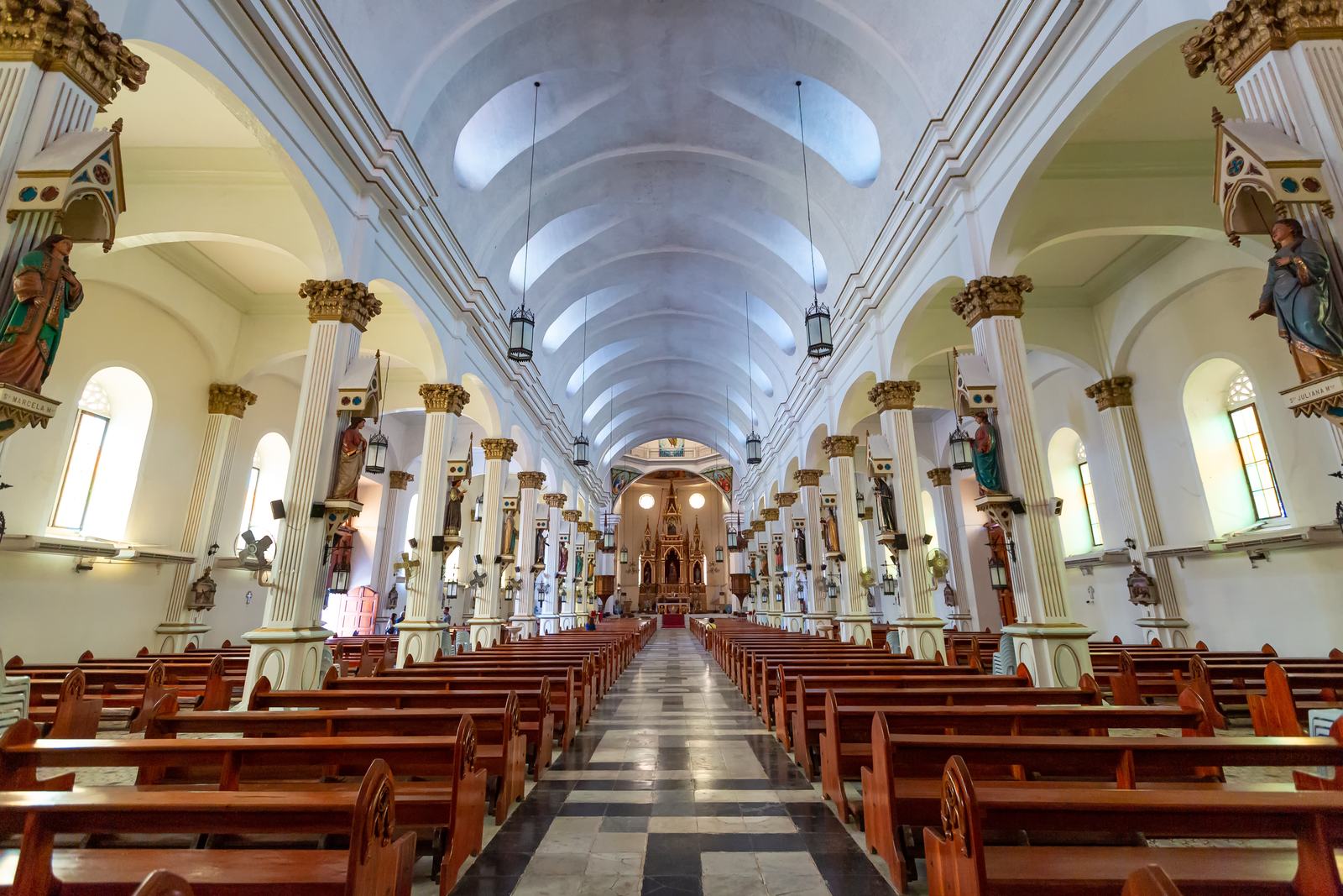 The white nave of an Iloilo church, columns and red pews leading to the altar.