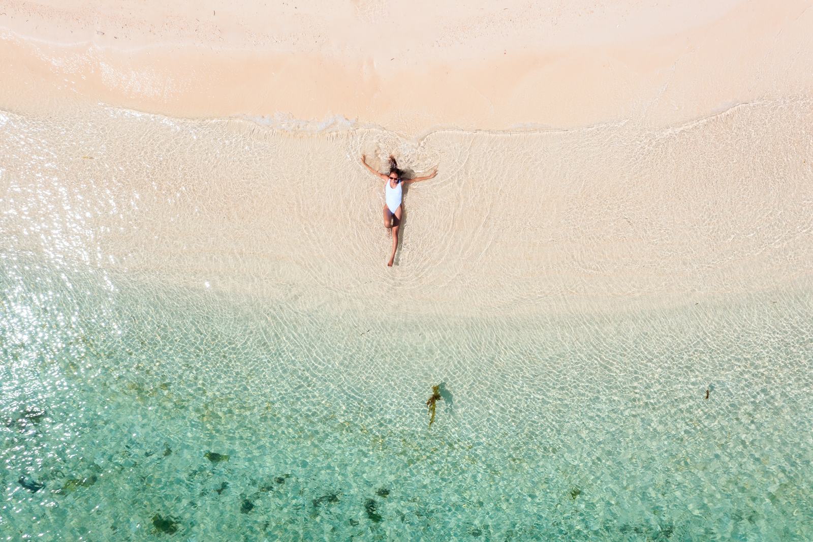 Clear shallows off a Siargao sandbar from above, a swimmer floating in the pale water.
